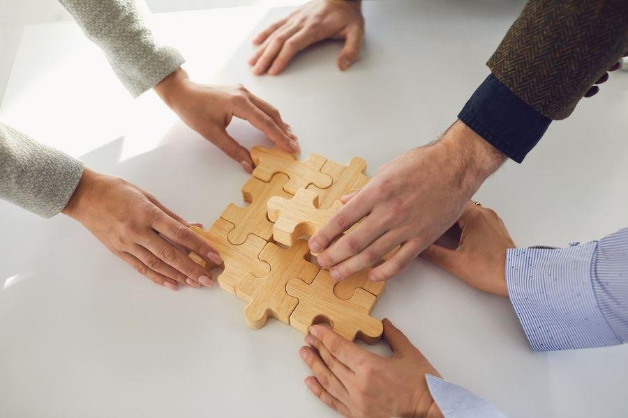 Mehrere Hände, die an einem Holzpuzzle zusammen bauen